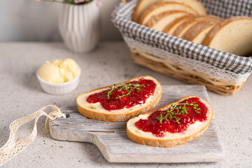 White bread slices with butter and raspberry jam on it, greens on wooden board, organic country sweet sandwich, homemade dessert. Copy space.