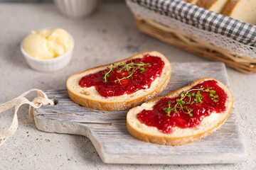 White bread slices with butter and raspberry jam on it, greens on wooden board, organic country sweet sandwich, homemade dessert. Copy space.
