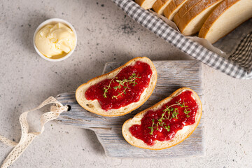 White bread slices with butter and raspberry jam on it, greens on wooden board, organic country...