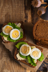 Black whole grain sliced bread with butter, salad leaves  and boiled eggs on wooden rustic table. Country, organic dietic opened sandwich. Copy space. Dark backgroound.