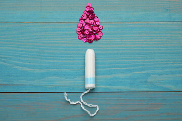 Tampon near drop made of pink sequins on turquoise wooden background, flat lay. Menstrual hygiene product
