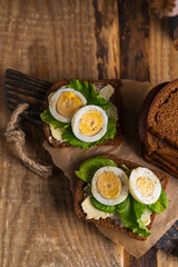 Black whole grain sliced bread with butter, salad leaves  and boiled eggs on wooden rustic table. Country, organic dietic opened sandwich. Copy space. Dark backgroound.