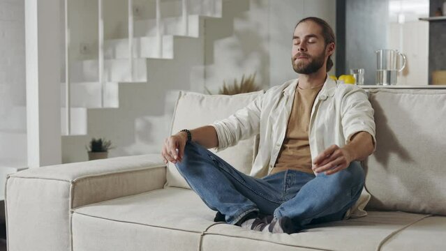 Handsome man meditating on couch in lotus pose