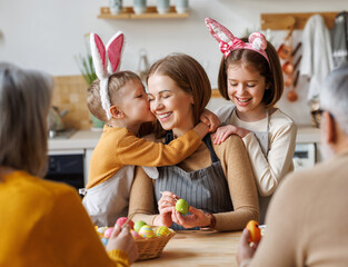 Cute little children embracing and kissing young happy mother while painting Easter eggs with family - 485657747