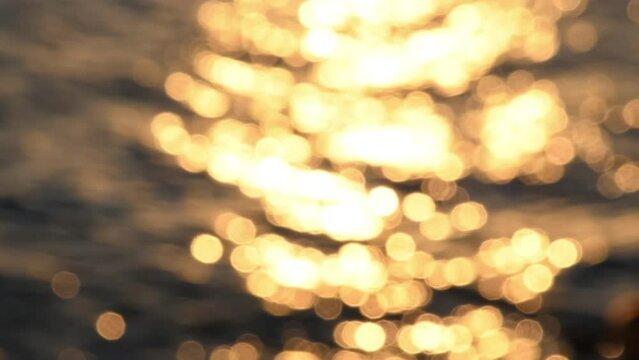 Blurred orange sea at sunset. Silhouette of woman with baby stroller walking along the promenade. Sun reflects and sparkles on waves with bokeh lights. Slow motion video. Motherhood theme.