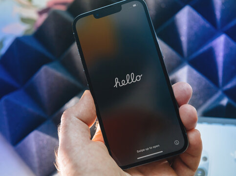 Paris, France - Sep 25, 2021: POV male hand holding new iPhone 13 Pro Max Sierra Blue color on tech background hero object with Hello mesage on the screen