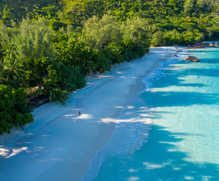 Aerial view of a person walking barefoot on the empty paradise beach of Anse Lazio, Grand Anse, Seychelles.