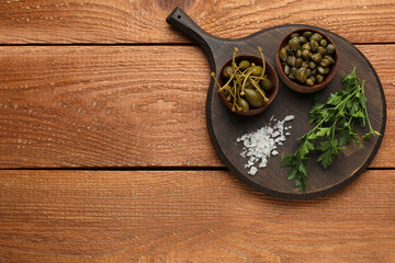 Delicious pickled capers, salt and parsley on wooden table, top view. Space for text