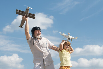 Grandfather and grandson hold plane and drone quad copter against sky. Child pilot aviator with plane dreams of flying.