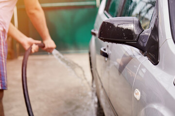 Man washing the car with water from under the hoses. Spring cleaning concept. Home routines. Caring...