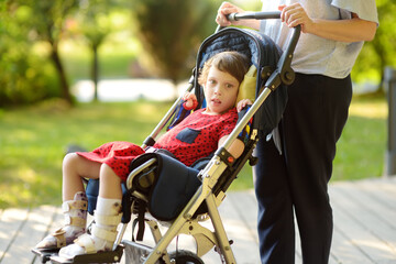 A woman with a disabled girl in a wheelchair walking in the park summer. On baby legs orthosis....