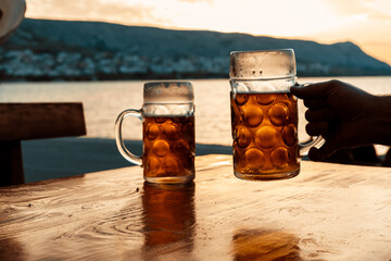 Cold beer in the hands, toast with a mug of beer on the coast in the sunset. Summer, Party, Holiday,	