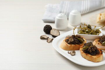 Delicious bruschettas with truffle sauce and caperberries on white wooden table. Space for text