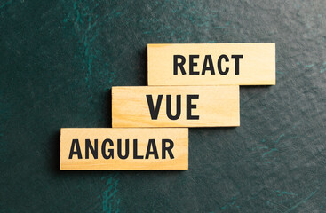 There is a blue notebook on a light gray background. Above are three wooden blocks with the words REACT VUE ANGULAR