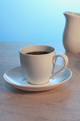 white cup of tea and milk jug on a wooden table on a light background