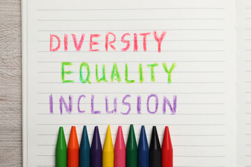 Notebook with words Diversity, Equality, Inclusion and wax pencils on wooden table, top view