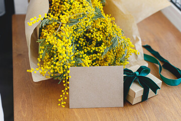 Stylish mimosa bouquet, gift box and greeting card on wooden background. Happy womens day and Happy...