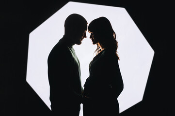 Silhouette of a stylish, smiling bearded man and a beautiful pregnant girl with a big belly on a white background in the studio.