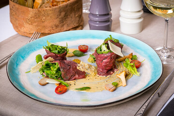 Gourmet beef appetizer with salad and wine, Elegant gourmet dish of beef rolls with fresh greens, mushrooms, cherry tomatoes, and cheese served on a restaurant plate with white wine.