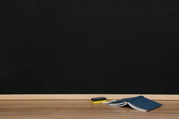 Open book, pieces of chalk and duster on wooden table near blackboard, space for text