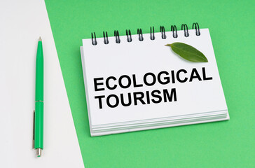 On a white-green background lies a pen, a leaf of a plant and a notepad with the inscription - Ecological tourism