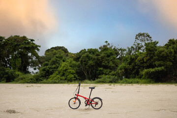 bicicleta dobrável na praia com exuberante natureza ao fundo 