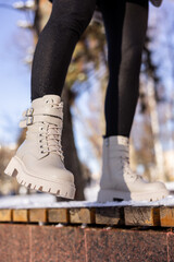 Woman in fashionable white boots on white snow, close-up. Women's legs in stylish winter leather boots