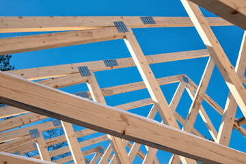 Wooden roof trusses on a new home construction project with blue sky in the background.