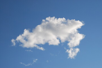 A small white cloud in a clear blue sky. Small cumulus clouds float across the light blue sky. They form a small group next to each other. Clouds of various shapes and sizes.