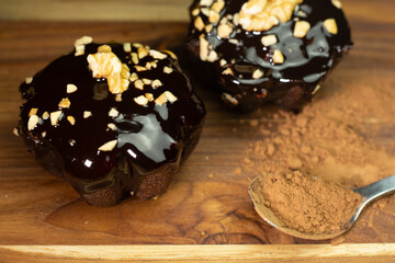 Two chocolate brownies on a wooden table next to a spoonful of chocolate powder