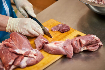 Cook cutting raw pork meat on wooden board in kitchen