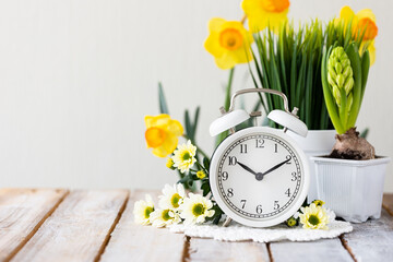 Spring change, Daylight Saving Time concept. White alarm clock and flowers on the wooden table - Powered by Adobe