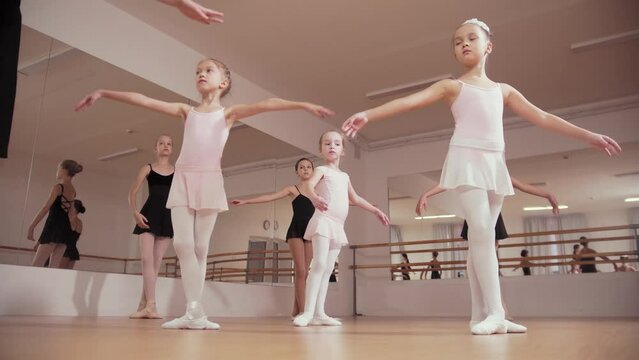 Ballet training - group of little ballerina girls make synchronous movements in the studio