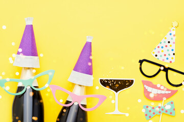 Holiday background with party props, masks, and champagne on a bright yellow background.