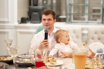 a man with a young son sits at a table and makes a toast into the microphone. 