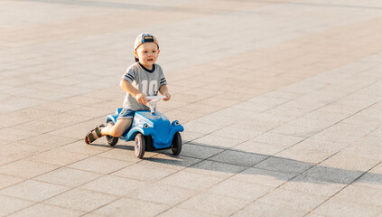 Little boy rides on a toy car in the park, happy child on a sunny summer day, driving a car outdoors