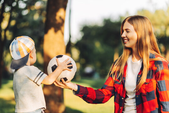 Happy Mom And Son Are Playing With A Soccer Ball While Sitting On The Green Grass In The Park. Image Of Family