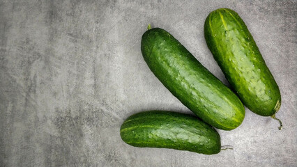 Three fresh green cucumbers on gray marble background.