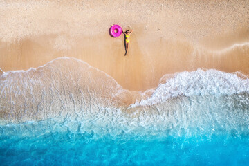 Luftaufnahme der liegenden schönen jungen Frau mit rosafarbenem Schwimmring am Sandstrand in der Nähe des Meeres mit Wellen bei Sonnenuntergang. Sommerurlaub auf der Insel Lefkada, Griechenland. Draufsicht auf schlankes Mädchen, klares azurblaues Wasser