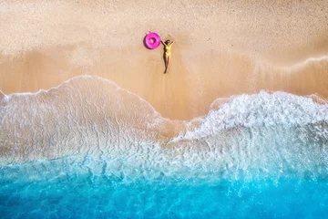 Luftaufnahme der liegenden schönen jungen Frau mit rosafarbenem Schwimmring am Sandstrand in der Nähe des Meeres mit Wellen bei Sonnenuntergang. Sommerurlaub auf der Insel Lefkada, Griechenland. Draufsicht auf schlankes Mädchen, klares azurblaues Wasser © den-belitsky
