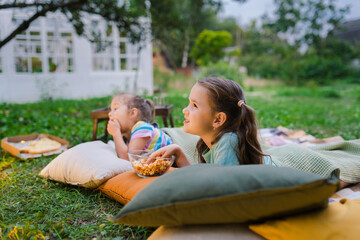 Side view of girls lying on blanket, eating homemade popcorn and watching film on DIY screen from...