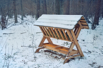 Wooden feed rack with forage for deer in winter forest.