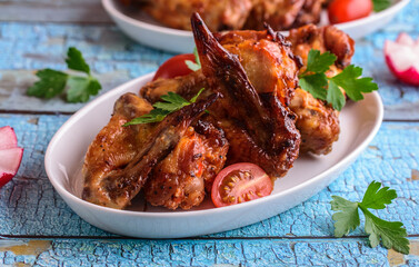 Baked crispy chicken wings in a white plate on a blue background.