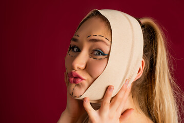 Plastic surgery. Beautiful young blonde woman touching her face with sketch and bandage on it....