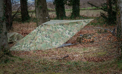 army soldier camouflage temporary tent cover erected amongst a woodland trees 