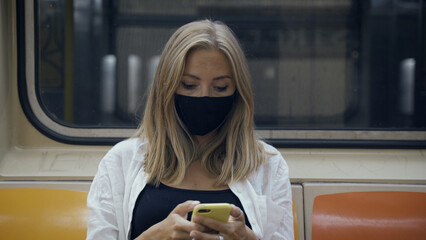 Woman in a black medical face mask to avoid the spread of coronavirus who is sitting alone in a...