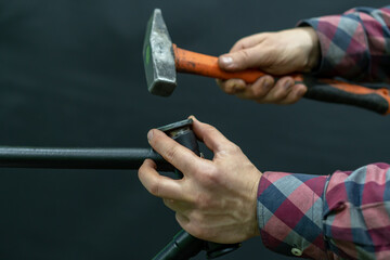 A bicycle mechanic with a hammer in his hands on a black background. The mechanic is holding an old...
