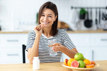 Young beautiful smiling caucasian woman holding vitamin pill and glass of water, looking at the camera and smiles friendly. Healthy lifestyle, healthy diet nutrition concep - Powered by Adobe
