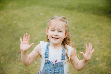 ittle blonde girl plays and shows hands. Child plays in the garden 