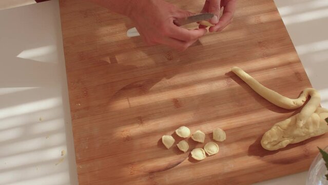 Close-up of hands making homemade pasta according to a traditional recipe from the southern Italian region. Orecchiette products are in the form of flattened discs no larger than 2 cm in size.